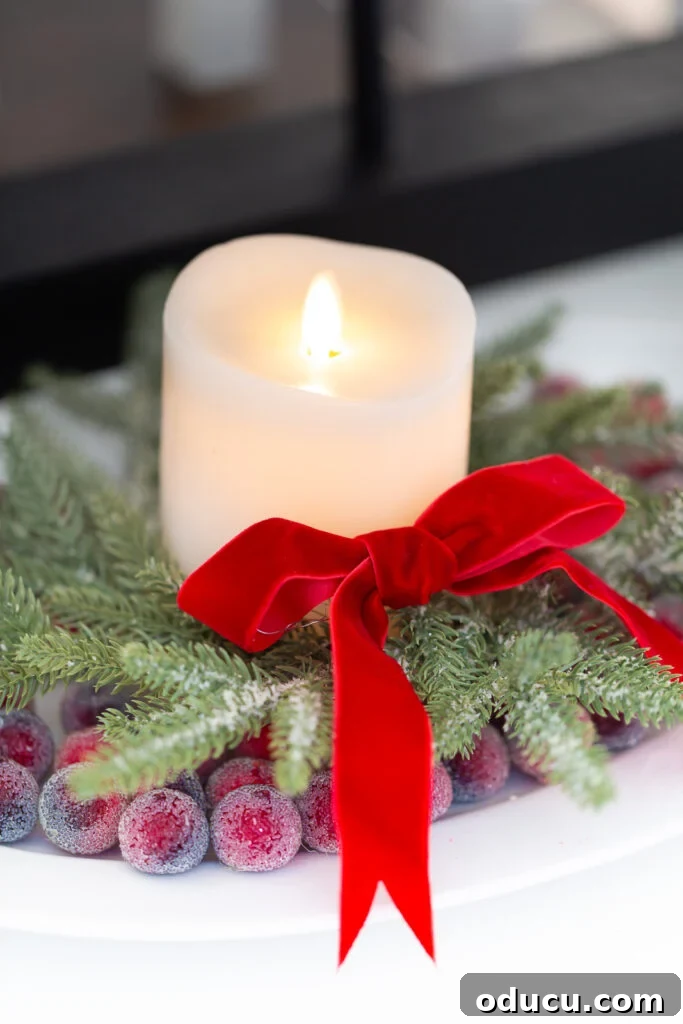 The Wreath Revelation You Need This Christmas 13 A close-up view of a white candle nestled within a small Christmas wreath on a platter, surrounded by glistening sugared cranberries, exuding festive charm.