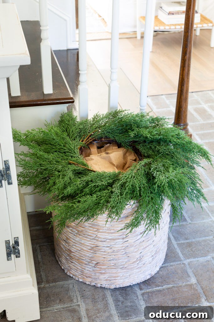 The Wreath Revelation You Need This Christmas 4 A lush greenery wreath is carefully placed on top of a large floor basket in a welcoming foyer.