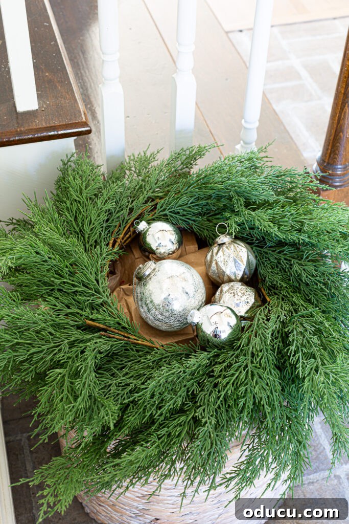 The Wreath Revelation You Need This Christmas 5 Sparkling silver Christmas ornaments are artfully arranged within the center of a greenery wreath, atop a floor basket.
