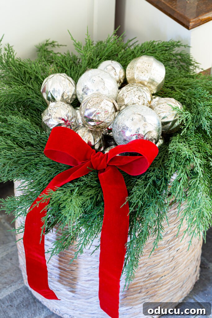 The Wreath Revelation You Need This Christmas 9 Close-up of a woven floor basket featuring nestled silver ornaments within a wreath, accented with a red velvet bow, creating a charming focal point in the foyer.