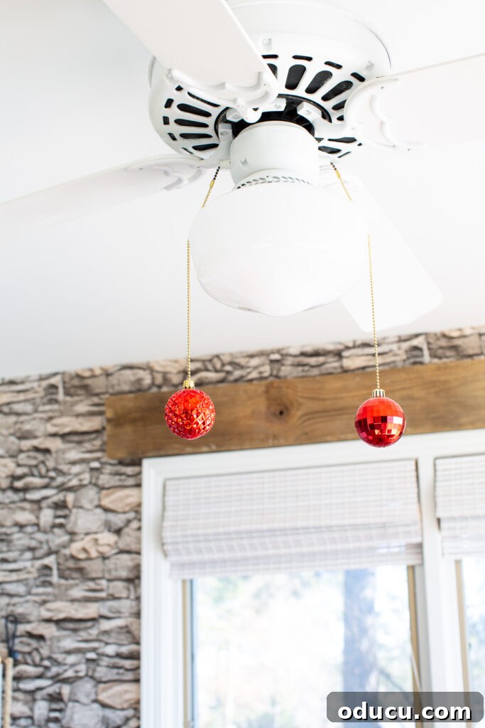 Christmas Decorating DIY in kitchen - adding shiny Christmas ornaments to the ends of the ceiling fixture pull chains.