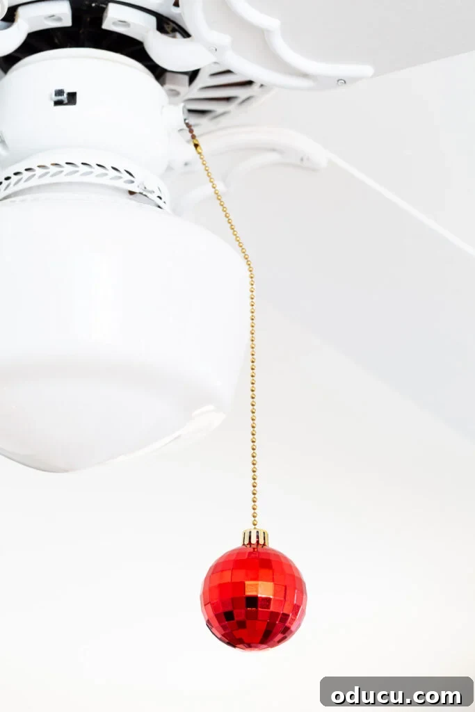 a red Christmas ornament added to the pull chain of a ceiling fan.