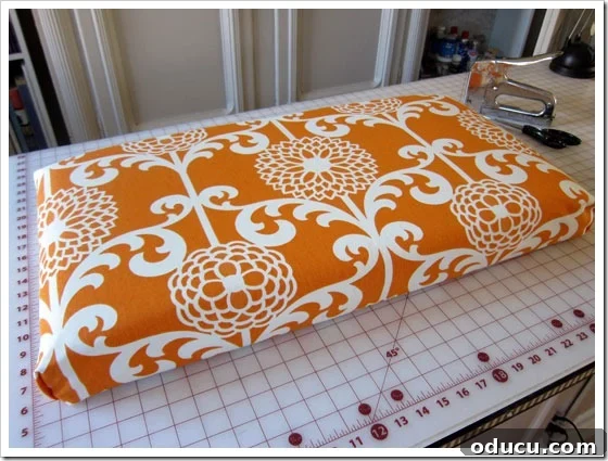 Ensuring proper fabric alignment on a foam cushion. Checking the fabric pattern alignment before final stapling of the cushion cover.