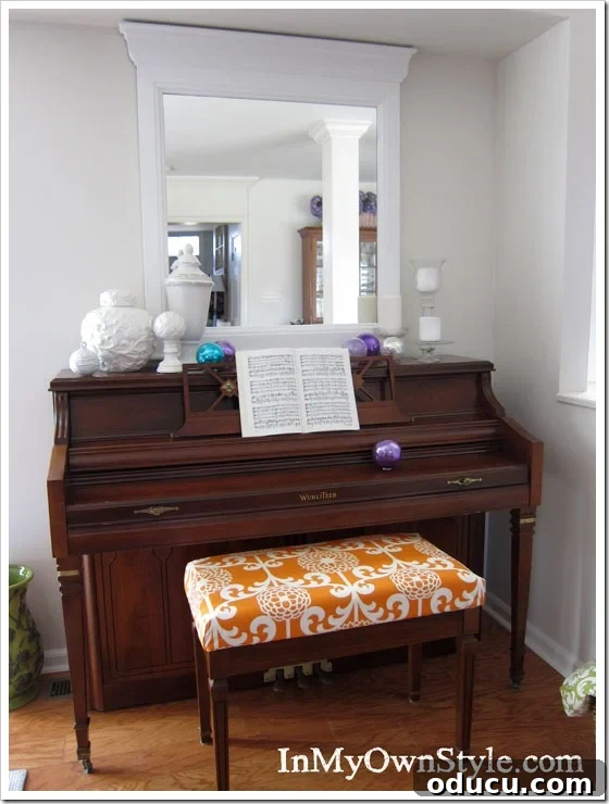 The complete look of a piano area with a custom no-sew bench cushion. The finished piano with its newly upholstered bench and a decorative mirror above.