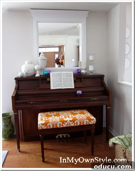 After shot of the piano bench with a custom no-sew fabric cushion cover. The piano bench after the no-sew fabric cushion cover has been added, showing a vibrant orange pattern.