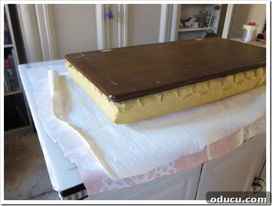 How to prepare for stapling fabric onto a bench cushion. Flipping the bench lid and fabric layers to begin stapling the cushion cover.