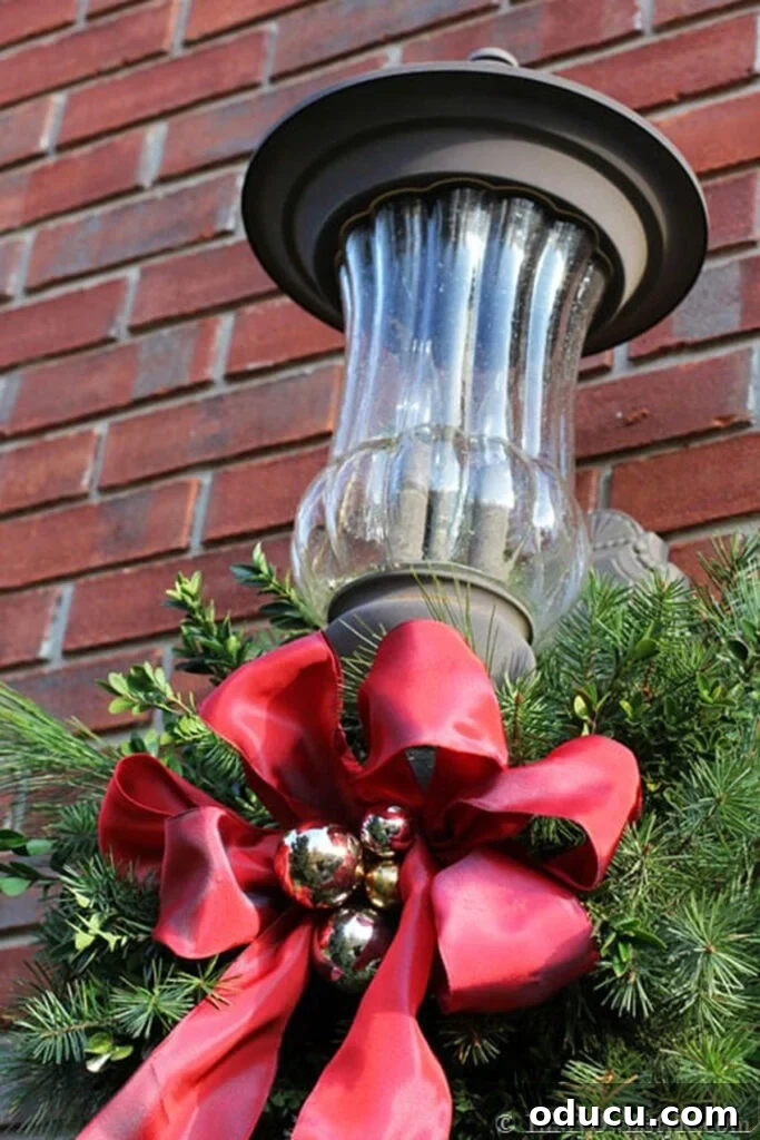 close up of an exterior front porch light decorated for Christmas using real greenery and red ribbon.