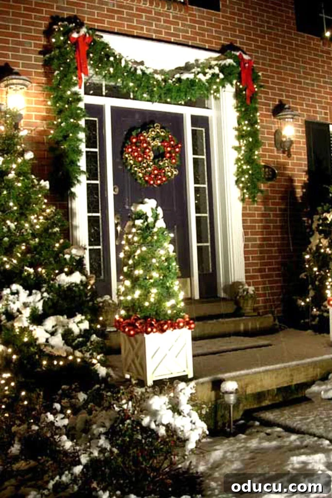 Front exterior of a brick home decorated for Christmas where lit garlands are hug and shrubs decorated with white lights.