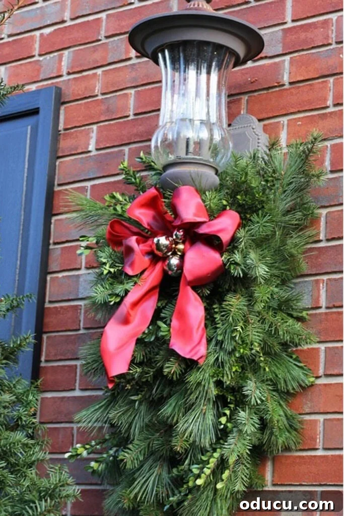Large front porch light decorated for Christmas using a clever DIY trick to hang greenery and attach ribbon.
