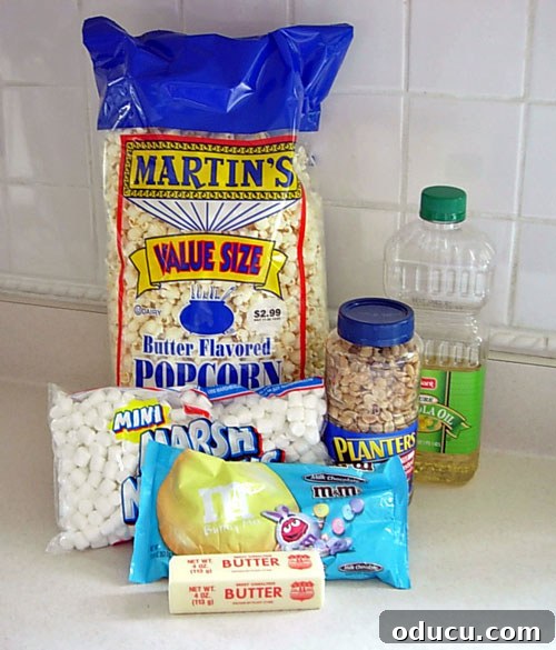 Popcorn-Cake-ingredients Popcorn cake recipe ingredients laid out on a clean kitchen counter, including marshmallows, butter, vegetable oil, popcorn, peanuts, and M&M's.