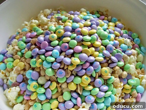 A big bowl filled with Popcorn-Cake-ingredients mixed-with-M&Ms A large mixing bowl filled with fluffy popped popcorn, crunchy peanuts, and colorful M&M's, ready for the marshmallow mixture.