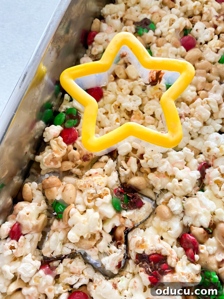 Festive Star Popcorn Cakes 5 Star-shaped cookie cutter being used to cut festive shapes from a sheet of marshmallow popcorn treats in a baking pan.