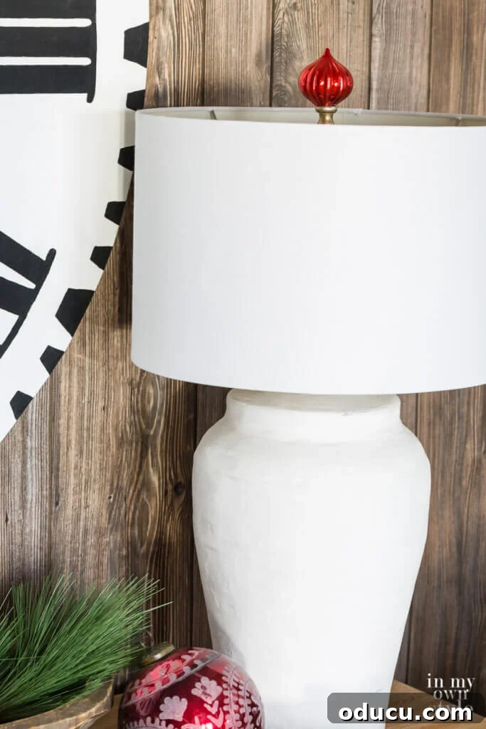 Thrifted Decorating Secrets Finding Your Home's Hidden Treasures 16 Holiday lamp finial idea. Close up of white table lamp with red Christmas ball ornament made into a finial above the lamp shade.