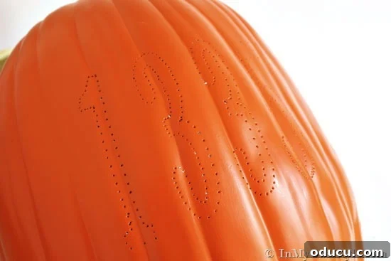 Technique for transferring house address numbers onto a foam pumpkin. Close-up of a foam pumpkin with a paper template being traced with a needle for carving house numbers.