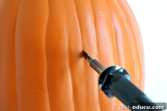 Demonstration of hot knife foam pumpkin carving technique. A hot knife carving tool being used to cut out house numbers on a foam pumpkin, following the dotted outline.