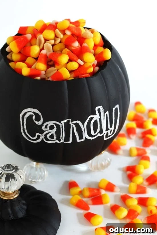 Finished foam pumpkin candy jar with cabinet knob feet and a chalkboard finish, filled with candy corn.
