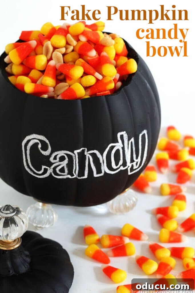 A beautifully decorated fake pumpkin transformed into a candy bowl, with 'CANDY' written on its chalkboard surface.