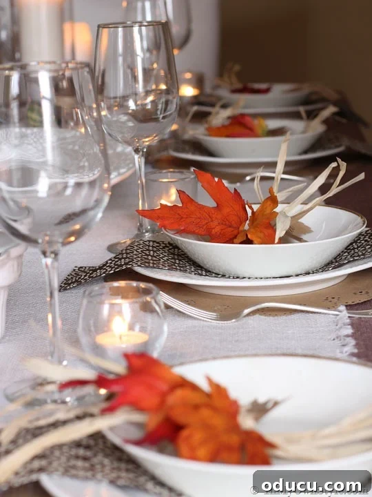 Thanksgiving table setting with wine glasses, white plates, and orange and brown accents, featuring leaf place cards.