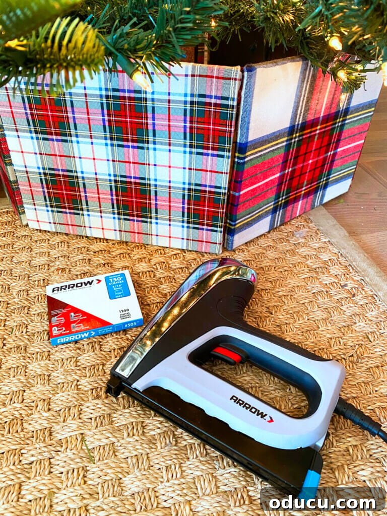 Upcycled Photo Frame Christmas Tree Skirt 14 A beautifully crafted plaid DIY tree collar rests on the floor next to an Arrow staple gun and a box of staples, ready for final touches in a festive setting.