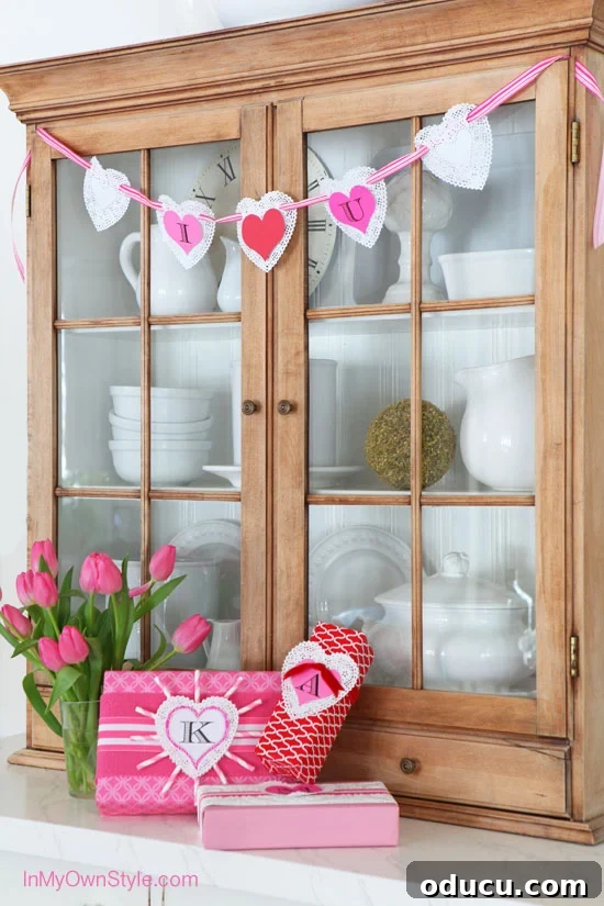 Heartfelt Initial Crafts: Free Valentine Printables 2 A charming DIY Valentine's Day banner crafted from paper doilies and custom initial heart printables, elegantly displayed on a rustic hutch. Perfect for festive home decor.