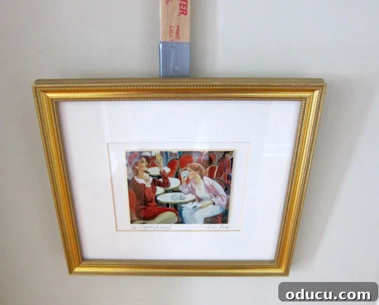 Instant Wall Decor: Hang Art & Mirrors Like a Pro 8 Holding the picture hanging gadget with a framed picture, positioning it on the wall.