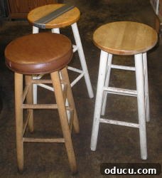 Three plain wooden stools, one with a worn brown pleather cushion.