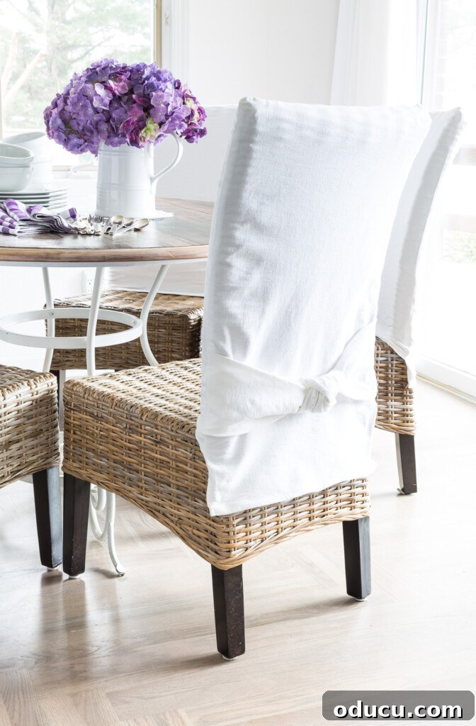 The Style Icon Who Solved My Decorating Dilemma 3 Wicker chairs around a round dining room table. Chairs have white slipcovers with a tied knot detail in the chair backs.