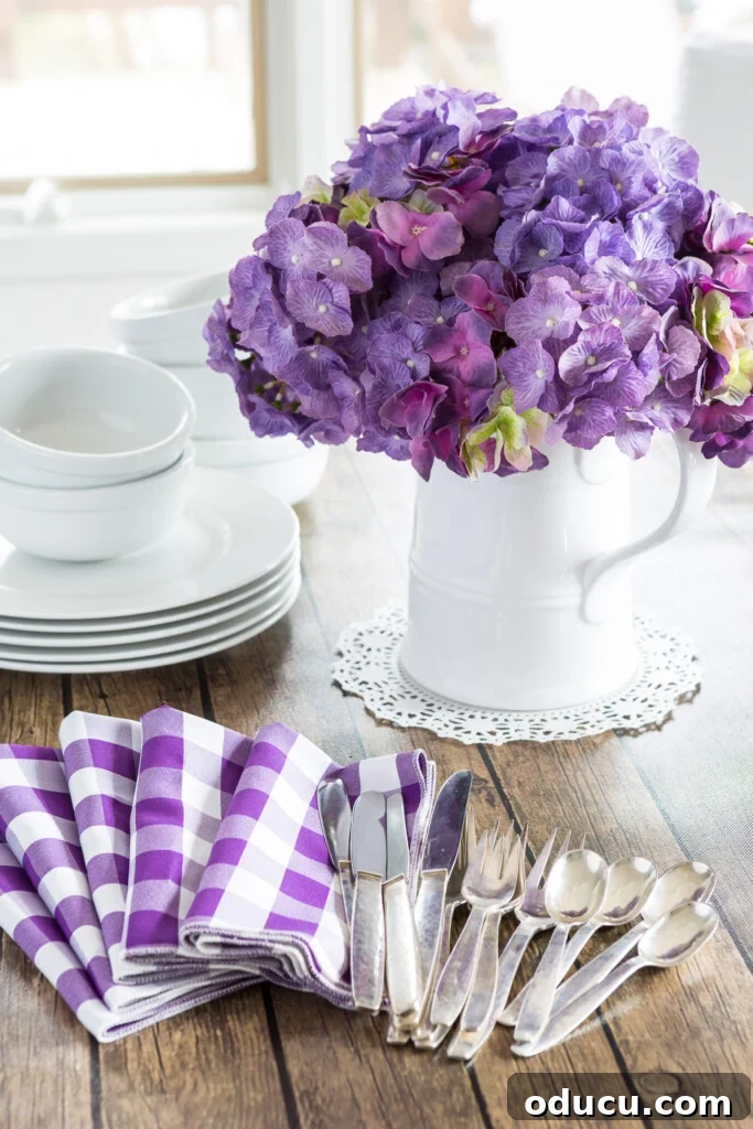 The Style Icon Who Solved My Decorating Dilemma 10 Decorating for spring using White dinnerware and white pitcher filled with purple hydrangeas on a wood table.