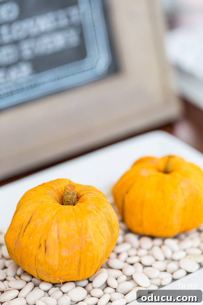 Effortless Autumn Pumpkin Decorating 11 A modern fall decor arrangement featuring a trio of paper pumpkins artfully styled on a tray of dried white beans, highlighting contrasting textures.