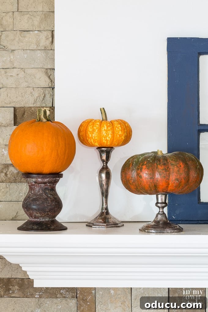 Effortless Autumn Pumpkin Decorating 17 Smaller pumpkins elevated on various candle holders and candlesticks to create a unique and artistic pumpkin topiary on a mantel.
