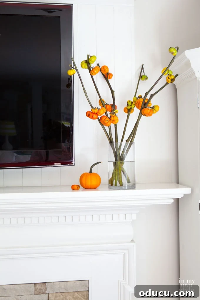 Effortless Autumn Pumpkin Decorating 6 Minimalist fall decor with a small pumpkin positioned next to a glass vase holding fall foliage stems, styled below a wall-mounted TV.