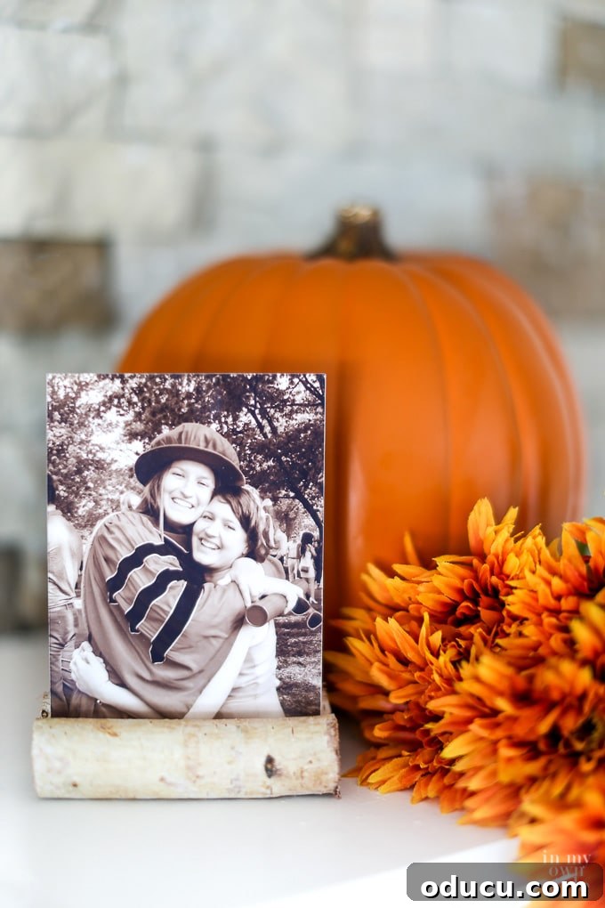 Effortless Autumn Pumpkin Decorating 7 An orange pumpkin serving as a striking backdrop for a rustic DIY autumn photo frame made with birch logs, enhancing a fall vignette on a mantel.