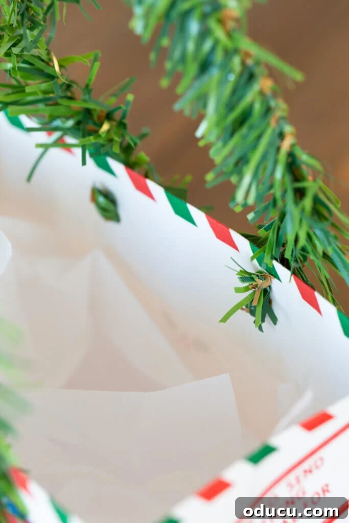 Detailed view of how to attach a pine garland tie to a gift bag to make a handle for the bag using punched holes.
