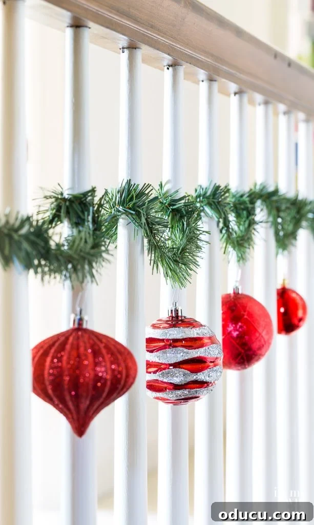 Christmas ornaments hung on staircase spindles with garland ties, creating a festive display.