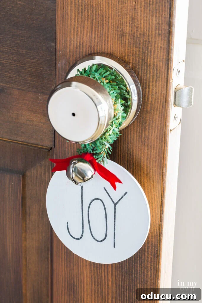 Wooden 'joy' ornament hanging on a doorknob, secured with a garland tie for a rustic touch.