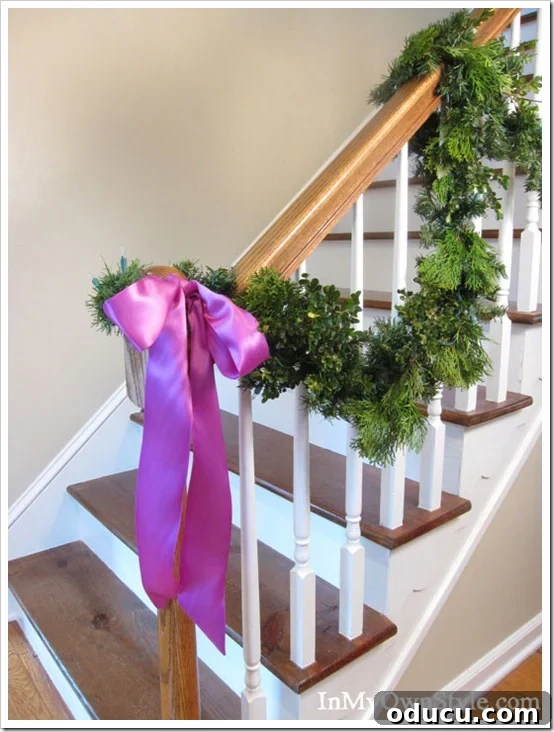 Beyond the Mantel: Clever Ways to Hang Christmas Stockings 3 Elegant staircase railing adorned with fuchsia satin ribbon and evergreen garland, showcasing a beautiful spot for Christmas stockings.