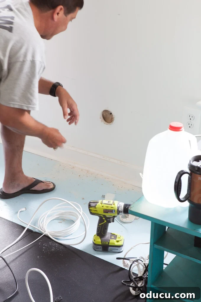 Installation tutorial on how to hide the cords on a wall mounted TV Man working on drilling lower hole in wall for TV cords to run through.