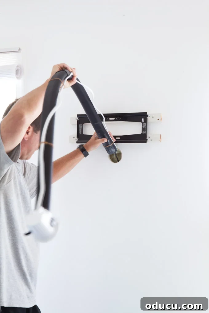 How to place plastic tube in wall to hide the cords on a wall mounted TV Man placing kit tube through the holes he drilled.