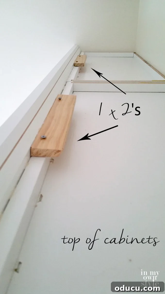 Mudroom Makeover: DIY Wall Cabinet Installation 6 Image showing crown molding with attached wood blocks being fastened to the top edge of wall cabinets using screws.