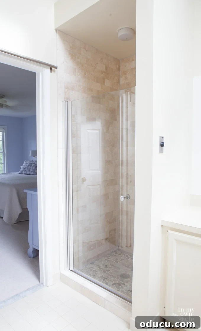 Luxury Master Shower Transformation 16 Completed stall shower in the master bath, featuring elegant tumbled stone tile walls, a pebble floor, and a clear glass door, showcasing fresh design ideas.