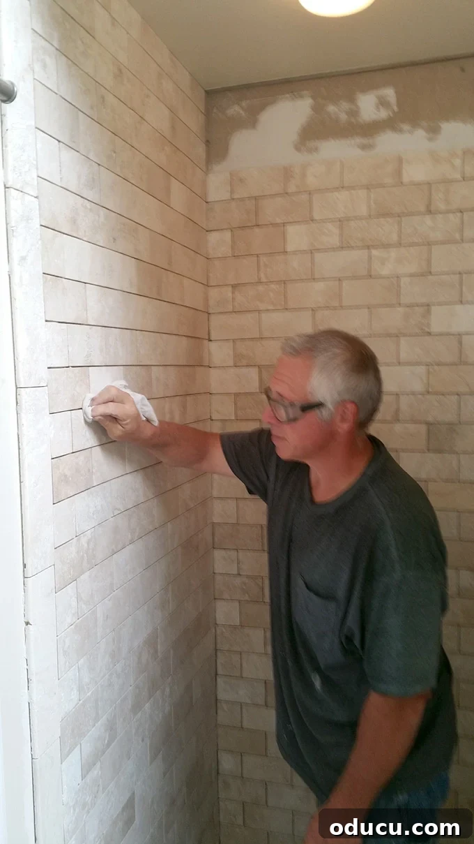 Luxury Master Shower Transformation 7 Skilled worker standing inside a shower enclosure, meticulously tiling the shower walls with natural stone tiles during the renovation process.