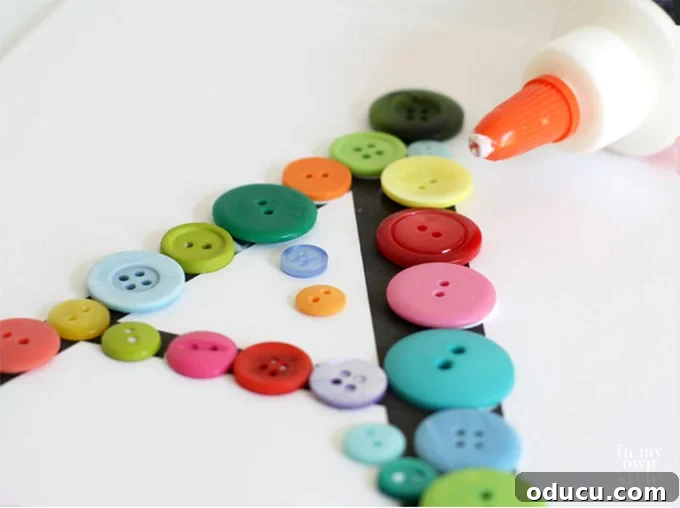 Create Custom Button Letter Wall Art 9 A hand applying white glue to the back of a button before placing it on the letter template.