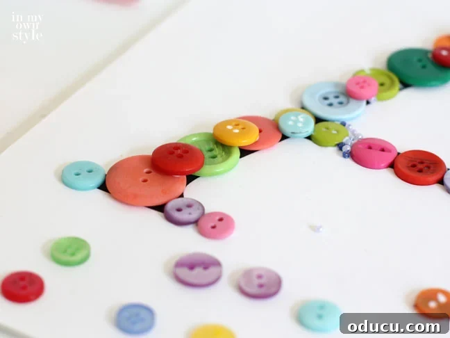 Create Custom Button Letter Wall Art 10 A close-up showing a second layer of colorful buttons being glued onto a printed letter, adding dimension.