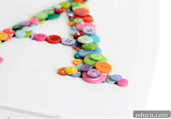 Create Custom Button Letter Wall Art 11 A detailed view of a partially completed button letter art, showing multiple layers of buttons and tiny beads filling spaces.