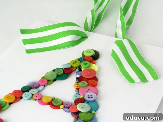 Create Custom Button Letter Wall Art 12 A hand threading a green and white striped ribbon through holes in the foam board of a button letter art piece.