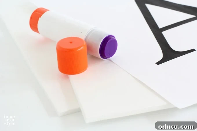 Create Custom Button Letter Wall Art 6 Hands gluing a printed letter template onto a foam board, showing the mounting process for button art.