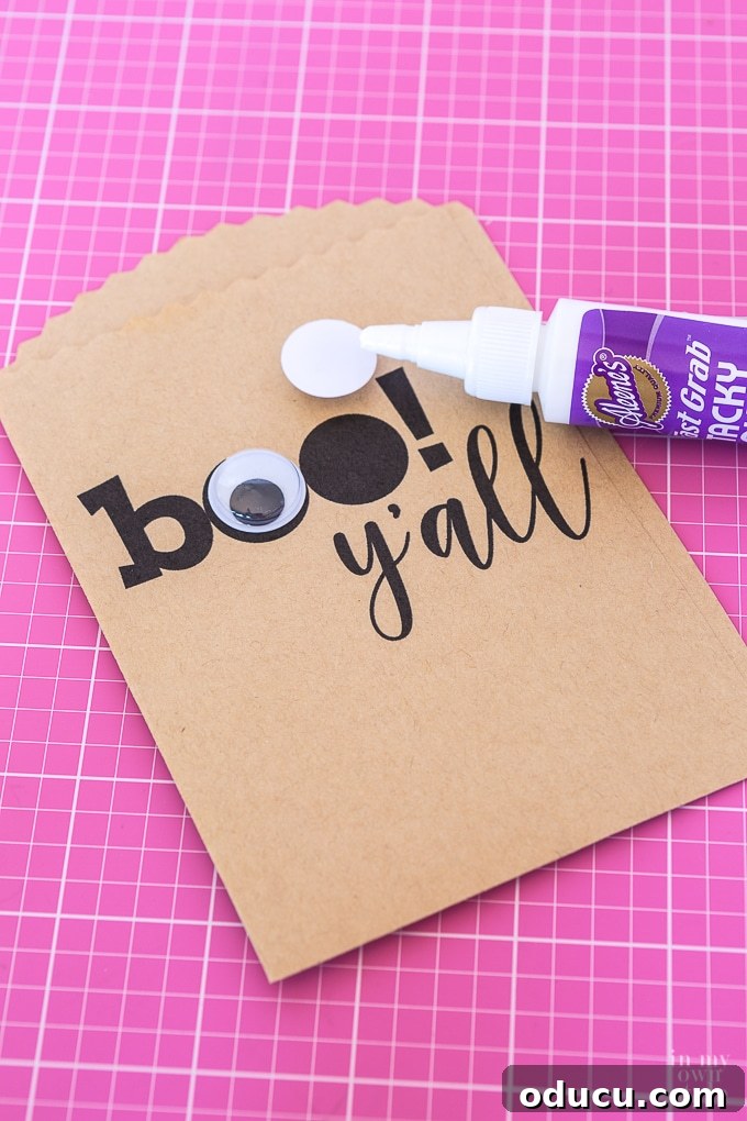 Spooktacularly Sweet Halloween Candy Pouches 13 Applying googly eyes to the 'Boo' lettering on a Halloween treat bag