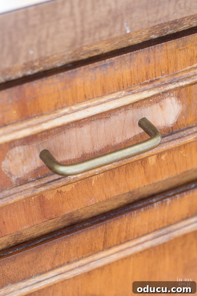 Close-up of old kitchen cabinet hardware, showing a dated pull on a wooden drawer.
