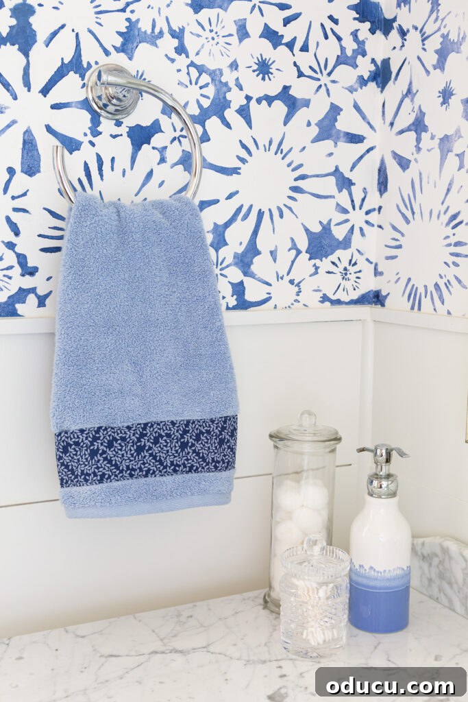 Elevate Your Bathroom With Towel Decor 14 A serene sky blue hand towel gracefully hanging from a towel ring, featuring a beautifully applied decorative fabric strip along its bottom edge for a charming embellishment.