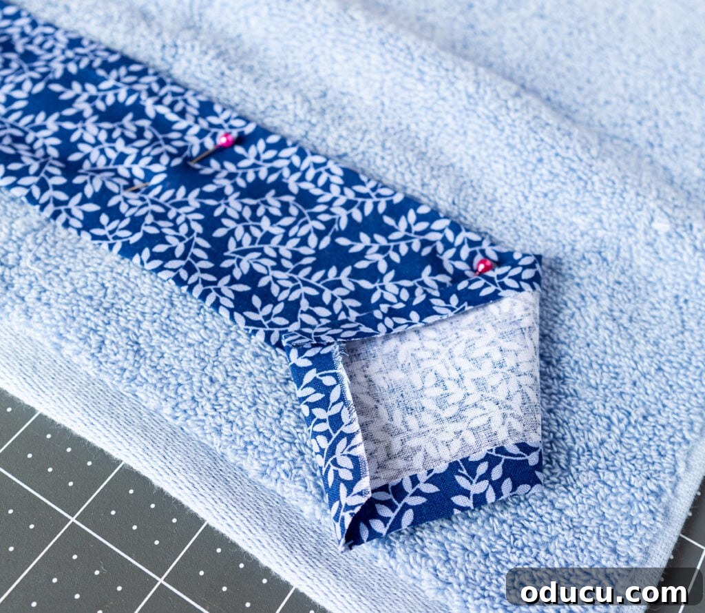 Elevate Your Bathroom With Towel Decor 15 A close-up shot of a hemmed fabric strip meticulously pinned to a towel, illustrating the crucial step before sewing for a neat and professional finish.